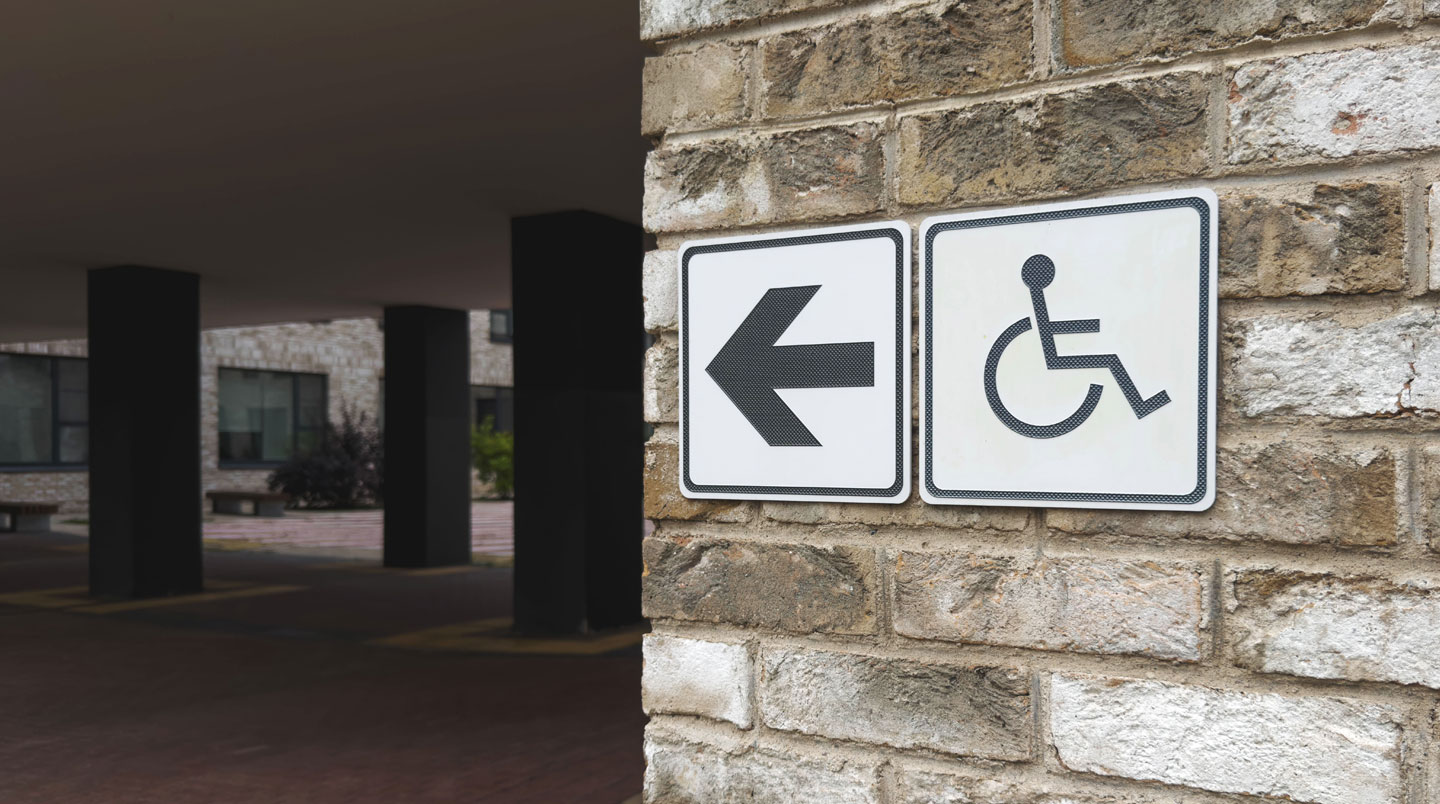 Panneau d'information municipale installé à hauteur accessible avec texte à fort contraste, photographié depuis le niveau d'un fauteuil roulant